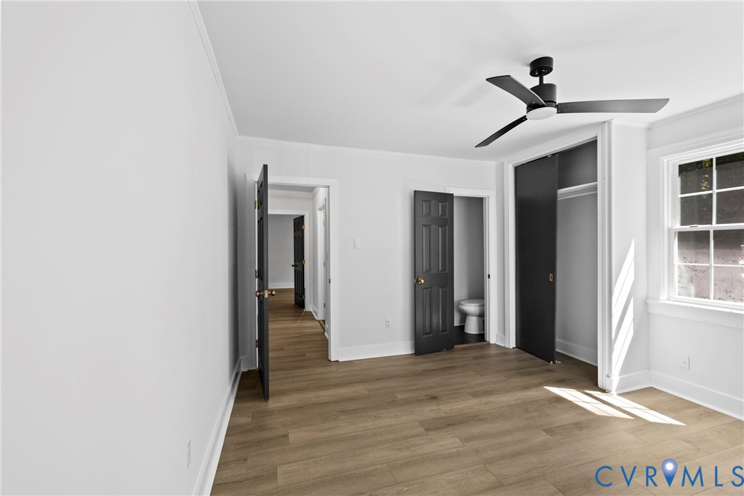 Wood-finish plank flooring, a modern black ceiling fan, white trim, and a window with multiple panes