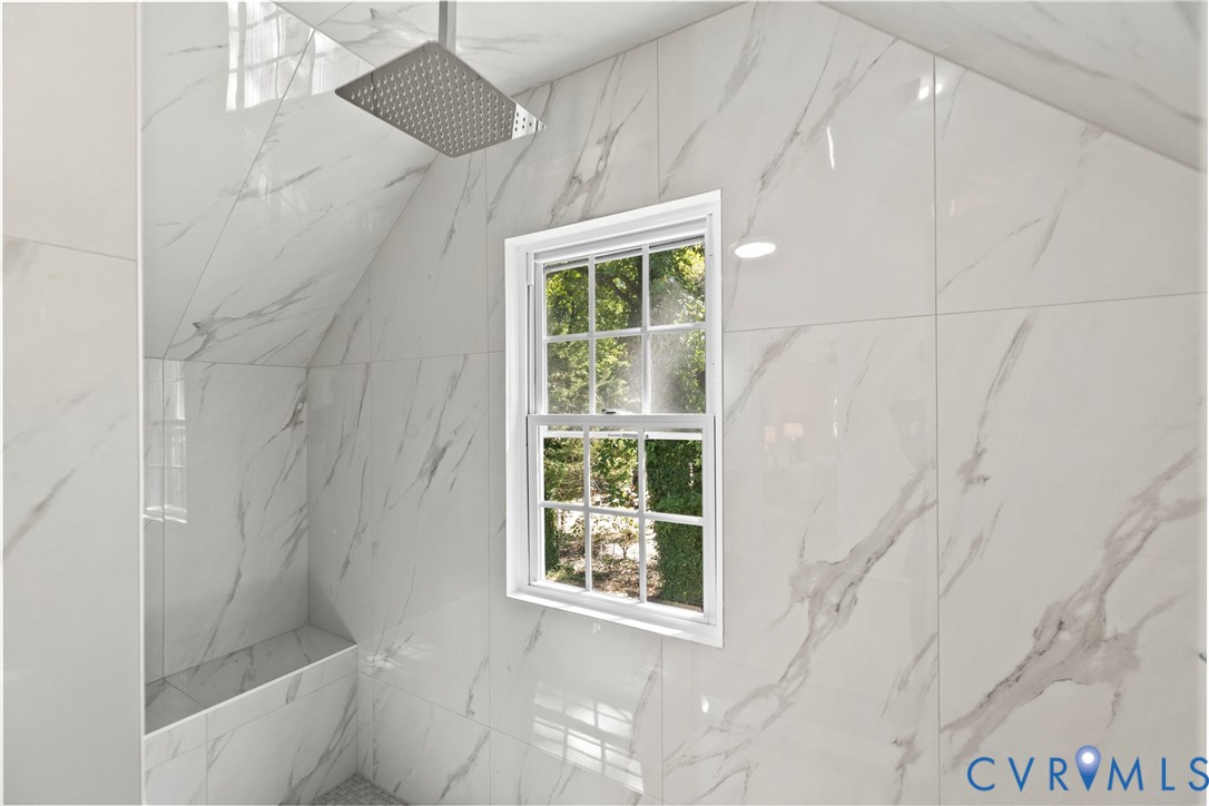 Shower featuring large format white and gray veined wall tiles, a built-in bench, and a rain showerhead