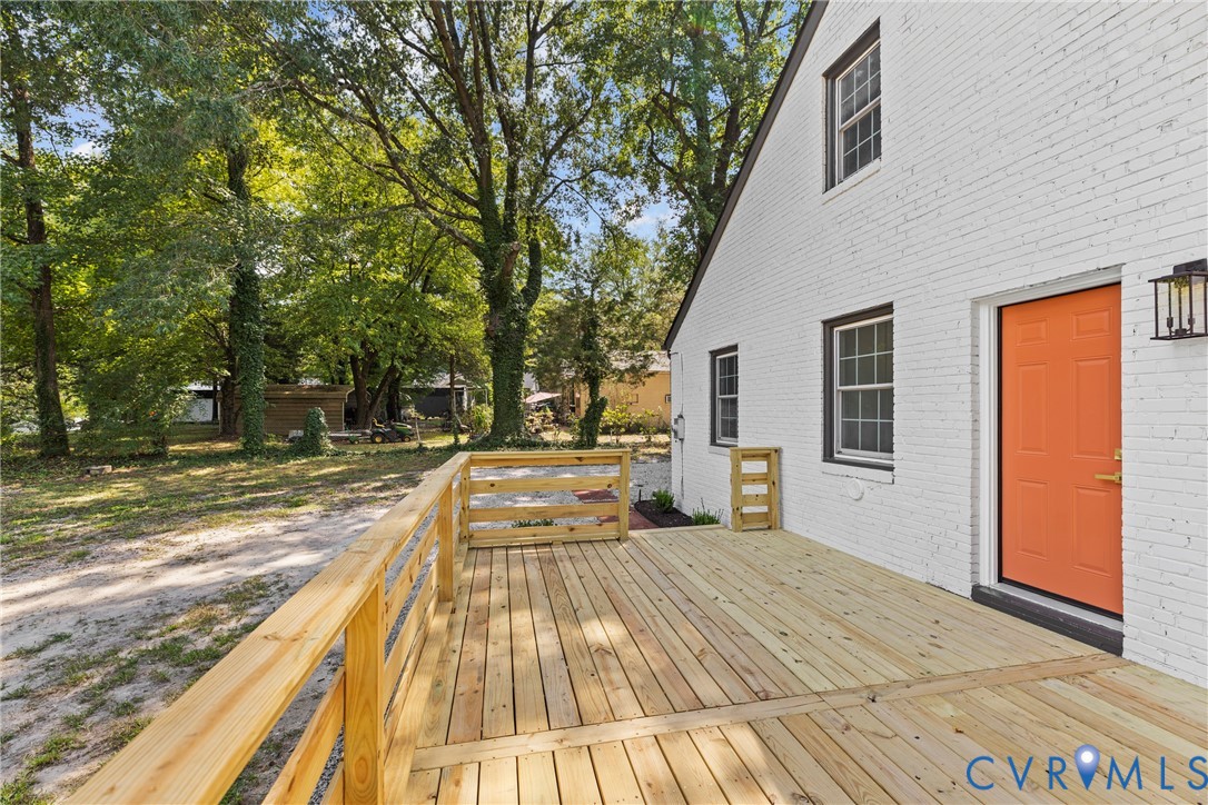 Expansive wood deck with a natural wood railing, white brick exterior, black window frames, and an orange entry door with a black exterior light fixture
