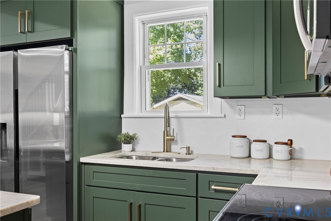 Kitchen featuring green shaker-style cabinetry, light-toned countertops, and a stainless steel refrigerator