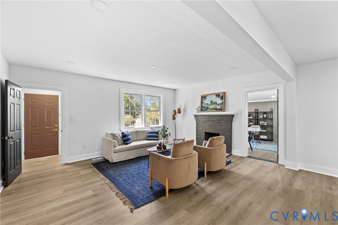 Spacious living area featuring wood-finish flooring, a brick fireplace with a white mantel, and recessed lighting