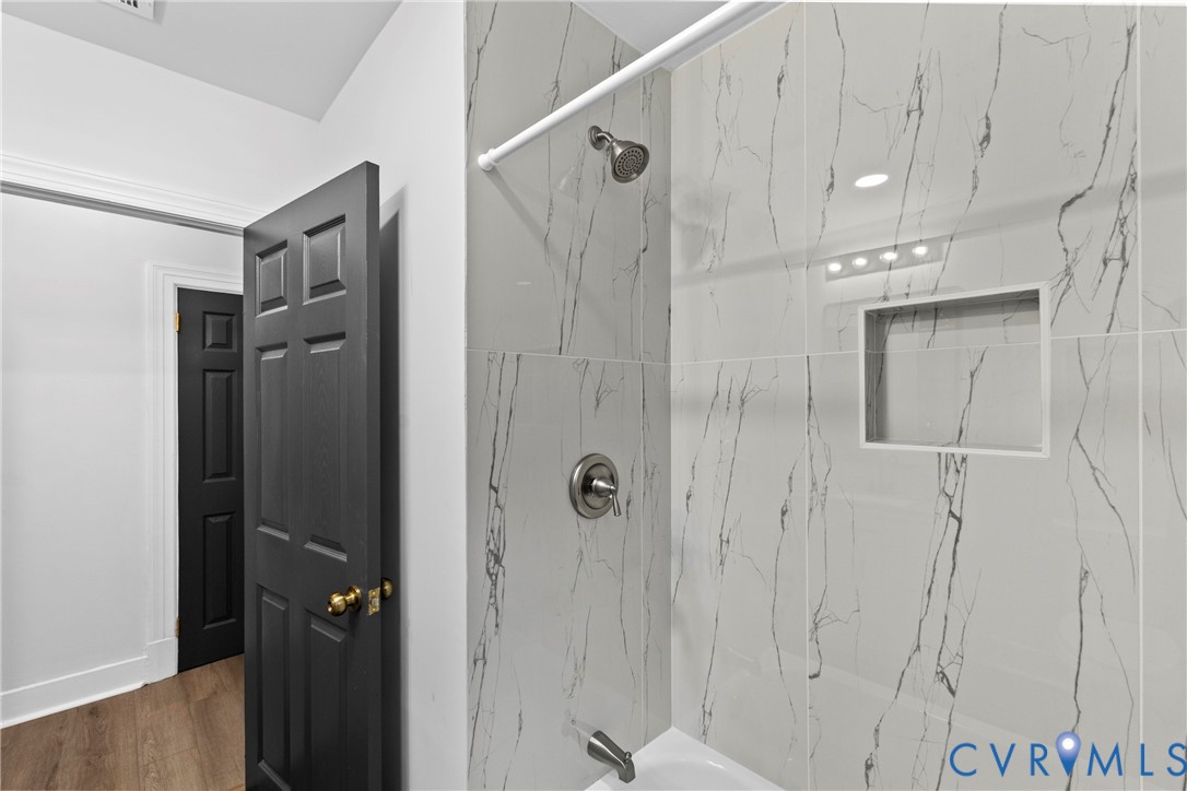 Bathtub with tiled surround, recessed shower niche, and ceiling-mounted lighting