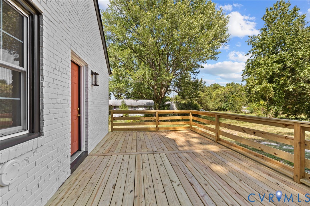 Expansive wood deck with a natural wood railing, white brick exterior, and a vibrant orange entry door