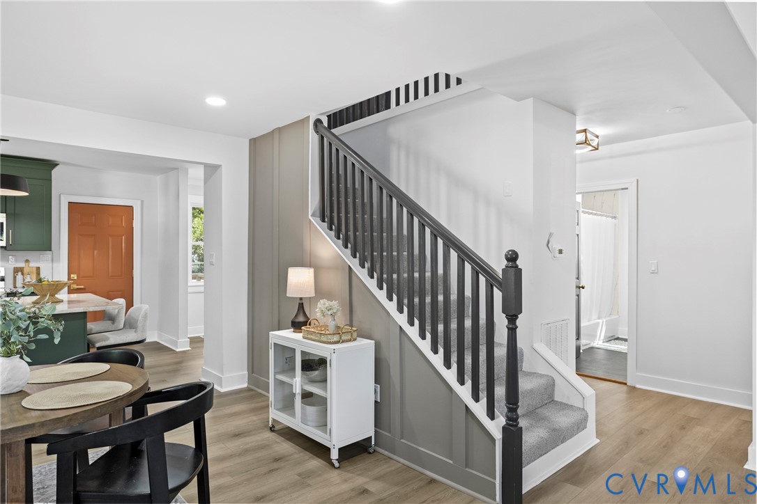 Gray board and batten accent wall, wood-finish flooring, recessed lighting, carpeted staircase with dark wood balusters, and a solid orange door