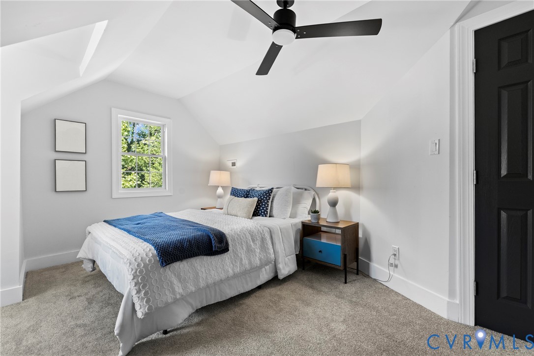 Sloped ceilings, window with natural light, wall-mounted light fixture, ceiling fan, and carpeted flooring