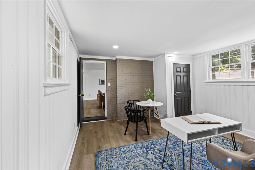 Wood-finish flooring, white beadboard wall paneling, painted brick accent wall, recessed lighting, and white-framed windows