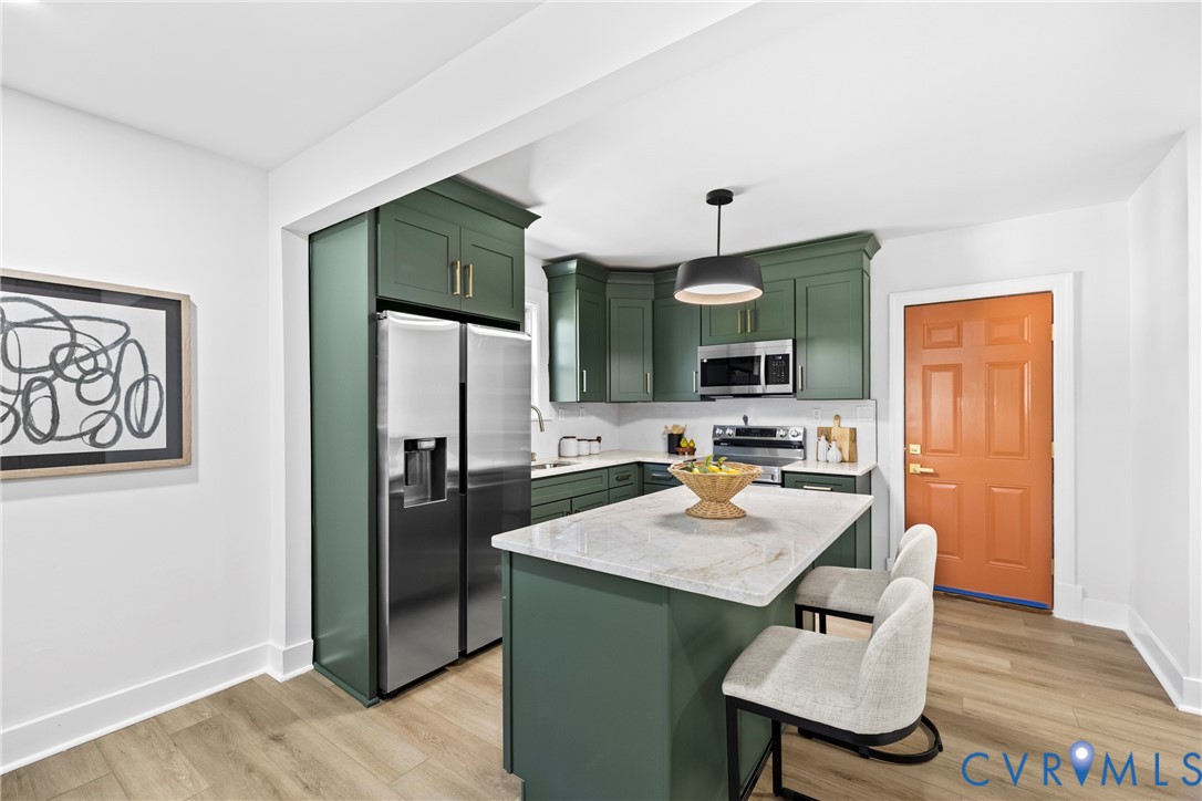 White shaker cabinets with gold-tone hardware, stainless steel appliances, central island with seating, pendant lighting, and wood-finish flooring