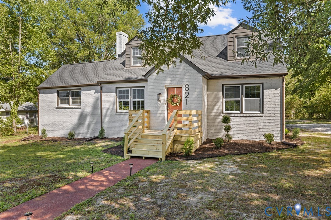White brick exterior with dark trim windows, dormer windows, and a newly constructed wood deck entryway