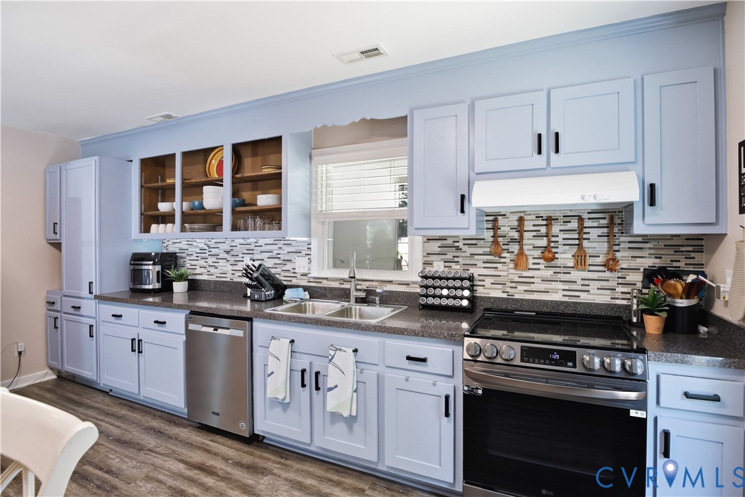 Light blue cabinetry, black hardware, stainless steel appliances, patterned backsplash, and wood-finish flooring