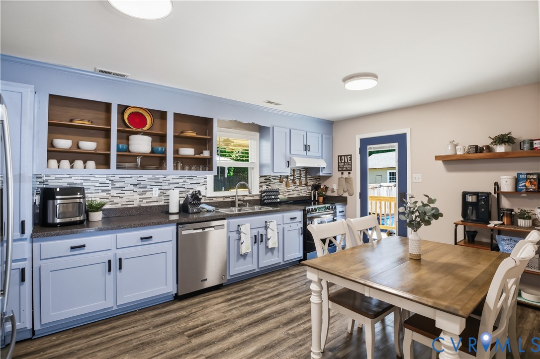 Kitchen featuring wood-finish flooring, light blue cabinetry, built-in dishwasher, tile backsplash, and a door leading to an exterior deck