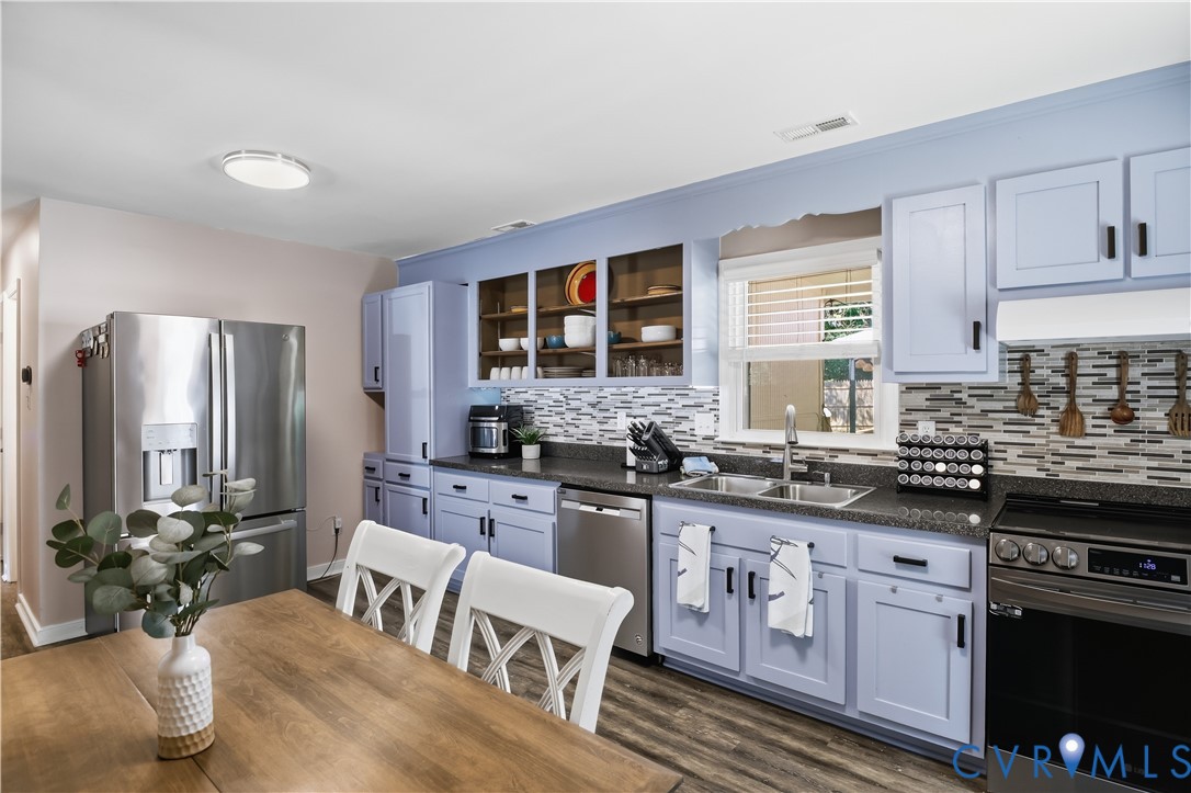 Stainless steel appliances, wood-finish flooring, two-tone cabinetry, tiled backsplash, and a double basin sink