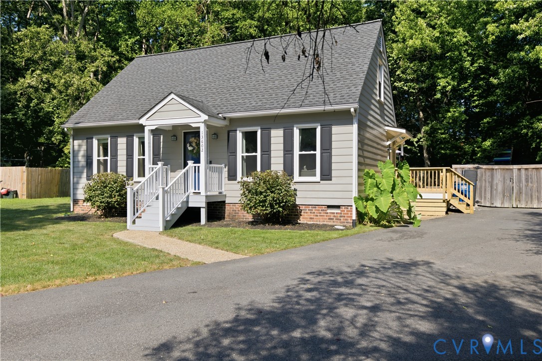 Gabled roofline, siding exterior, front porch with white railings, paved driveway, and a wood deck