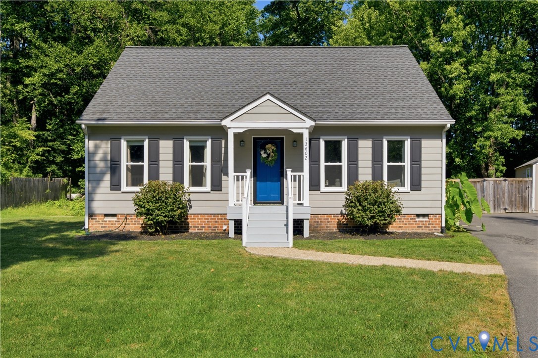 Exterior featuring light gray siding, dark gray shutters, a vibrant blue front door, a front porch with white railings, and a neatly manicured lawn