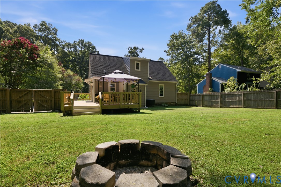Expansive backyard featuring a manicured lawn, a built-in fire pit, and a multi-level wood deck