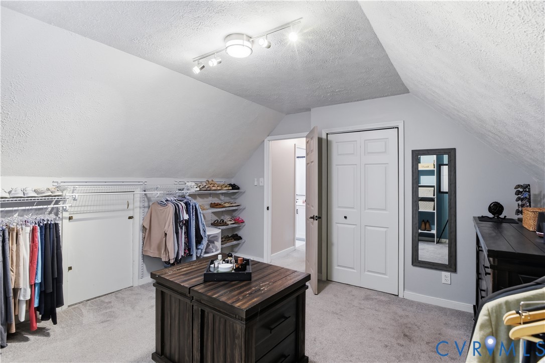 Carpeted flooring, vaulted ceiling, track lighting, bi-fold door, and built-in closet shelving