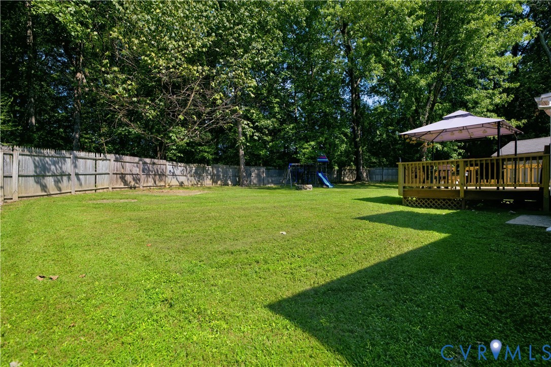 Expansive fenced backyard featuring a manicured lawn, mature trees, and a spacious wood deck