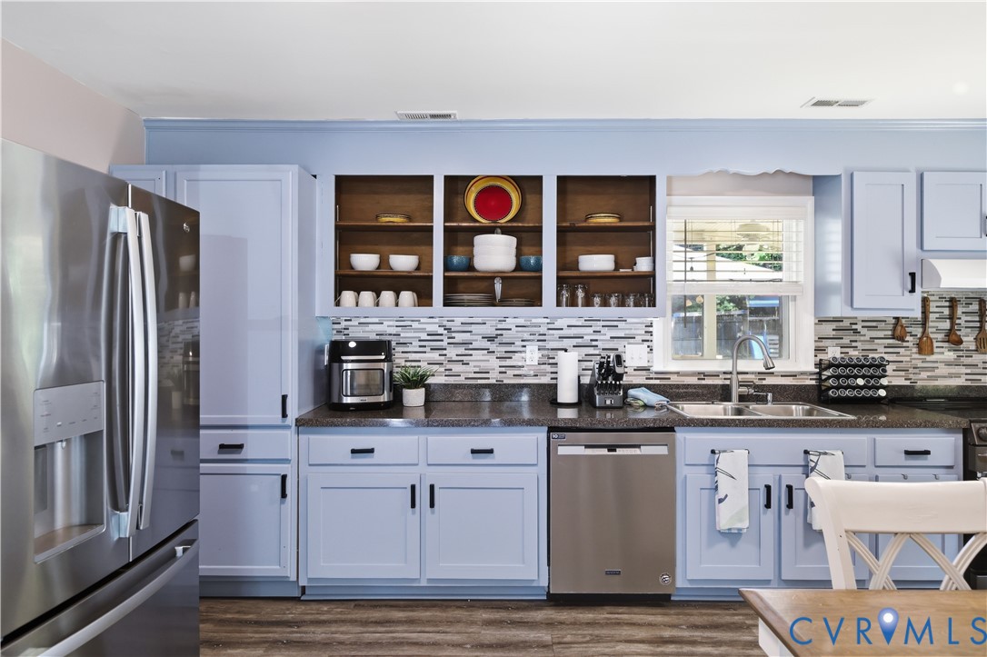Stainless steel appliances, light blue cabinetry with dark hardware, mosaic tile backsplash, solid surface countertops, and wood-finish flooring