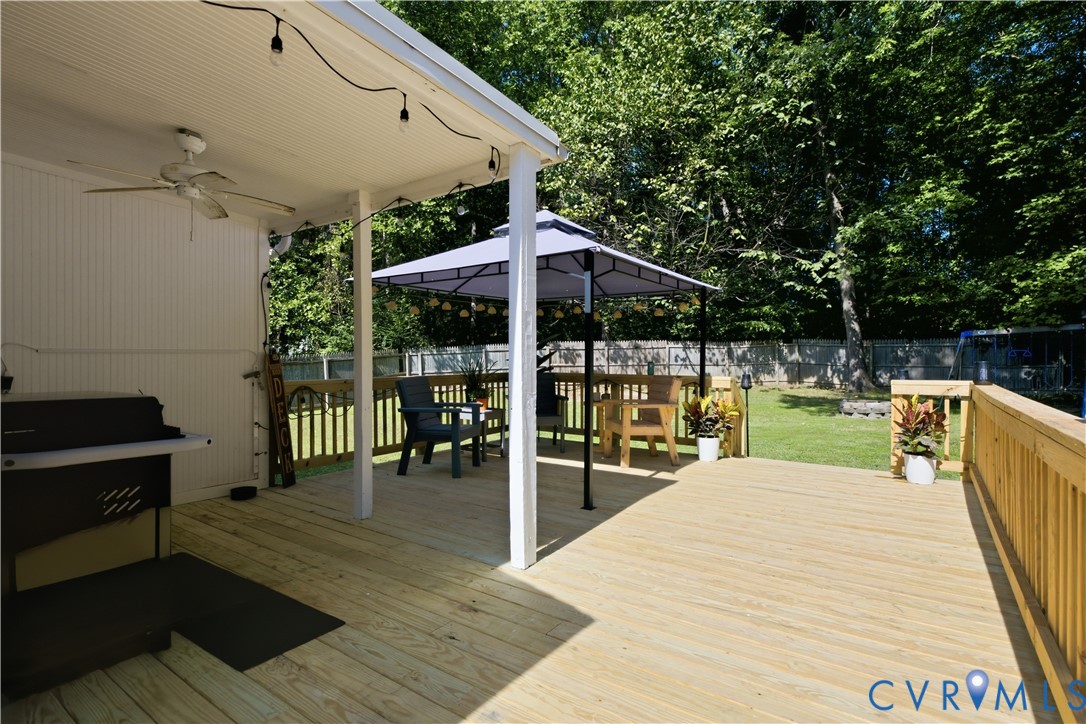 Expansive wooden deck featuring a covered patio, ceiling fan, and string lighting