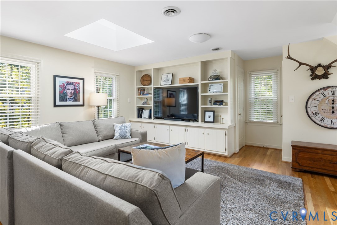 Integrated built-in cabinetry with shelving, wood-finish flooring, recessed lighting, skylight, and multiple windows with blinds