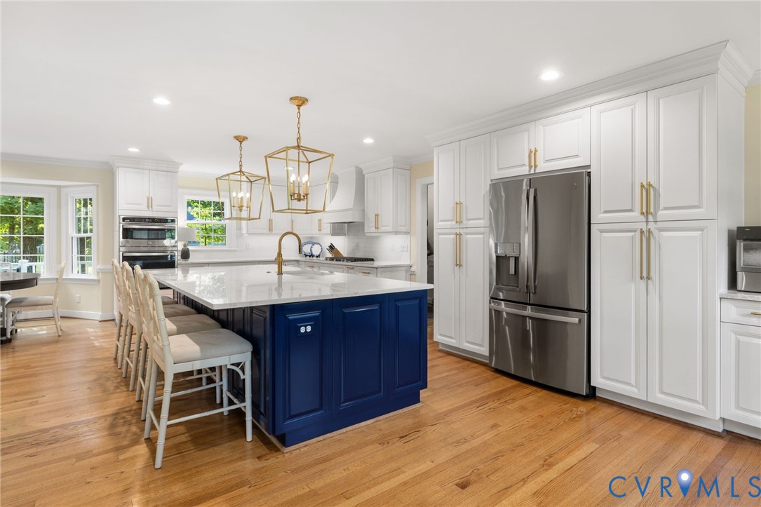 White shaker-style cabinetry with gold-tone hardware, a large blue island, stainless steel refrigerator, wood-finish flooring, and recessed lighting
