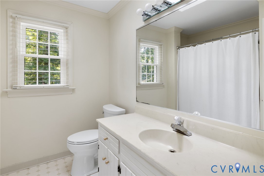 Full bathroom featuring a single vanity with an integrated sink, a toilet, a window with horizontal blinds, a shower with a curtain rod, and tile flooring