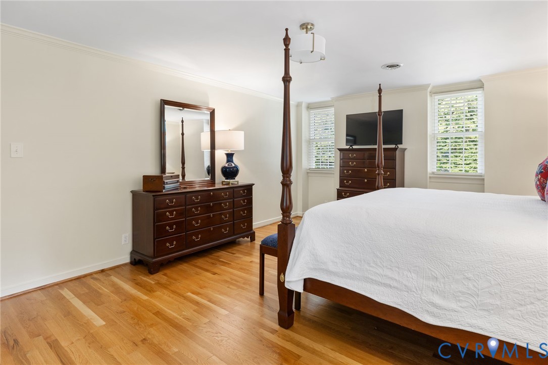 Wood-finish flooring, multiple windows with blinds, a ceiling-mounted light fixture, and crown molding