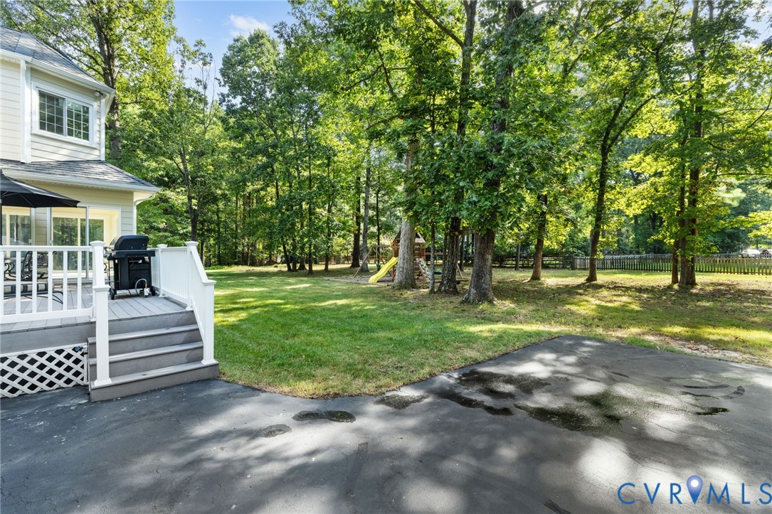 Expansive lawn bordered by mature trees and a wood fence, with a multi-level deck featuring white railings and steps