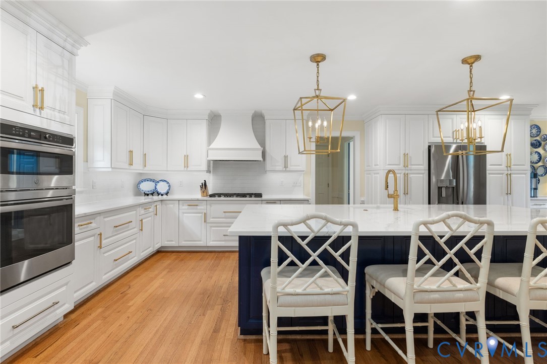 Spacious kitchen featuring an island with seating, white cabinetry, integrated stainless steel appliances, and wood-finish flooring