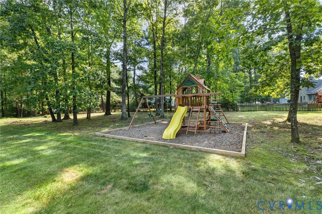 Expansive backyard with a wooden playset featuring a yellow slide, swings, and natural wood chip ground cover