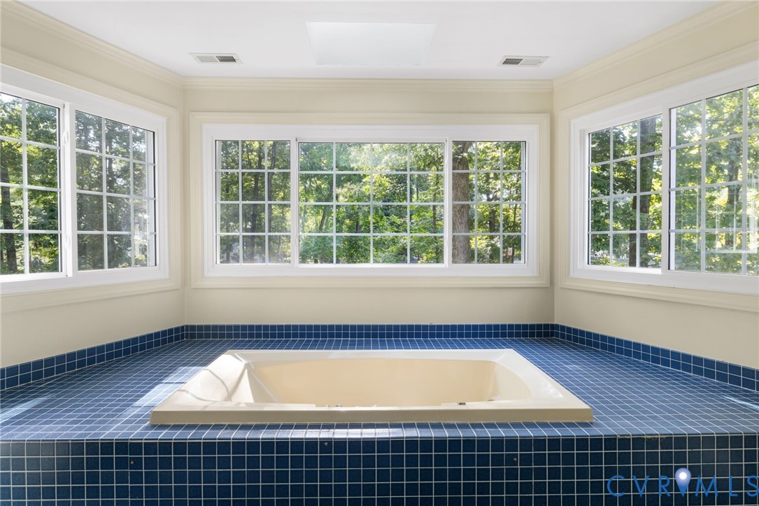 Recessed soaking tub set in a blue mosaic tile surround, surrounded by multiple grid-pattern windows