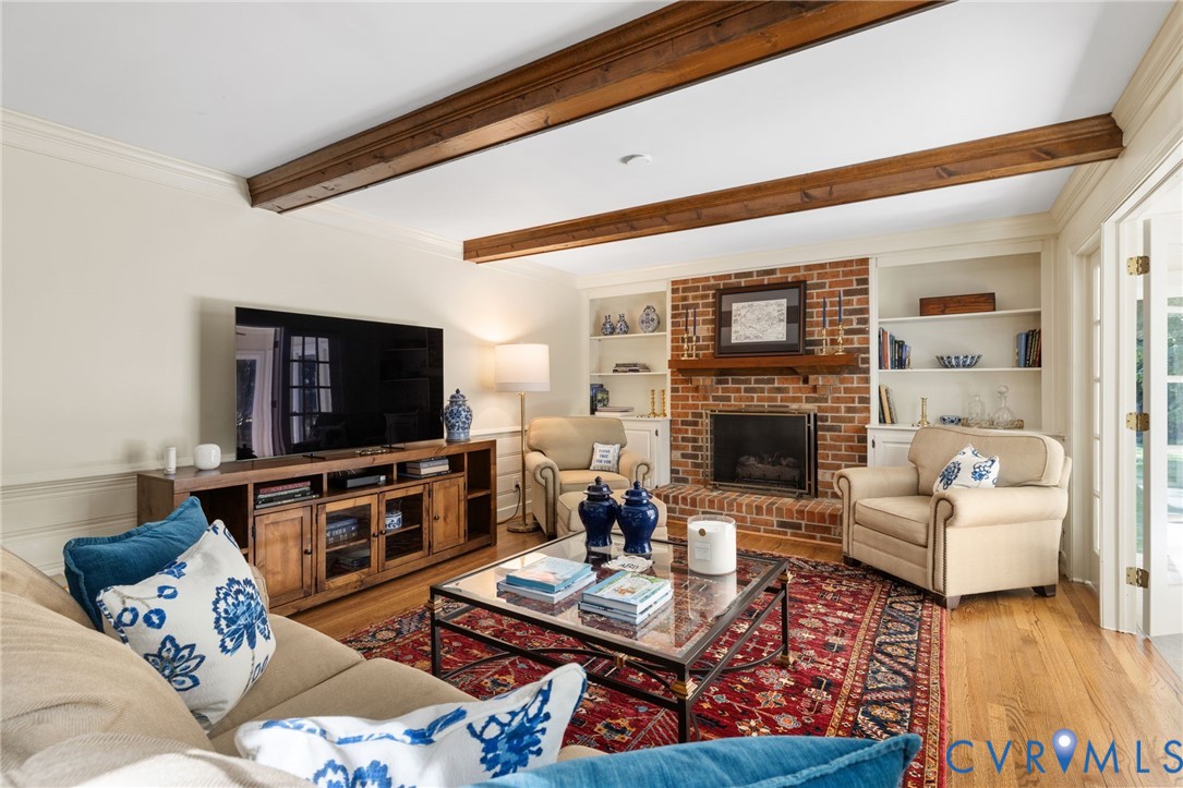 Exposed wood ceiling beams, brick fireplace with mantel, built-in shelving, wood-finish flooring, and French doors