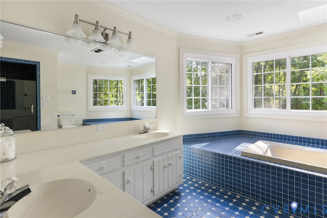 Dual vanity with integrated sinks, built-in soaking tub, blue tile flooring, tiled shower enclosure, and multiple windows