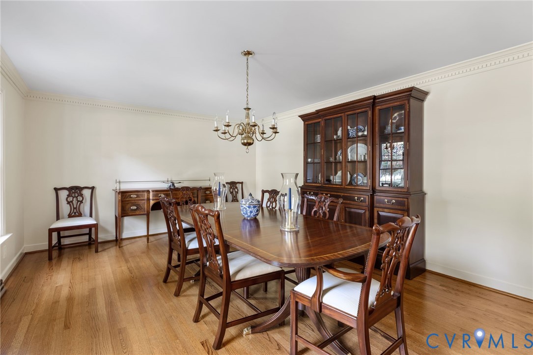 Hardwood flooring, crown molding, and a brass chandelier illuminate this dining space