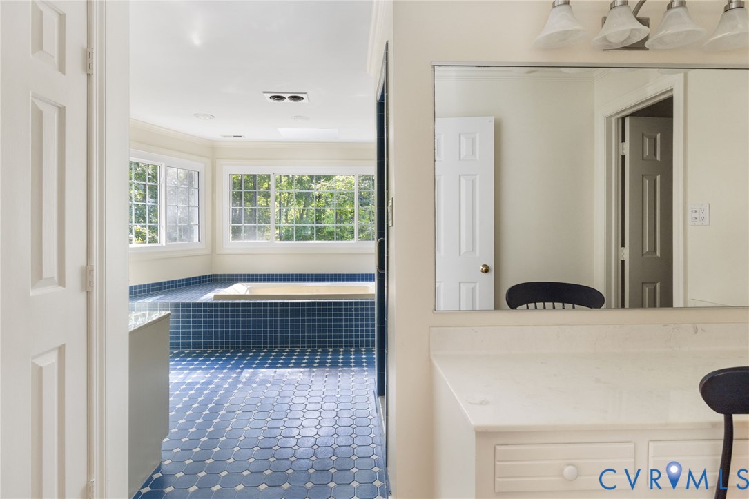 Built-in soaking tub with blue mosaic tile surround, multiple windows with grid patterns, recessed lighting, and a vanity with a built-in dressing table