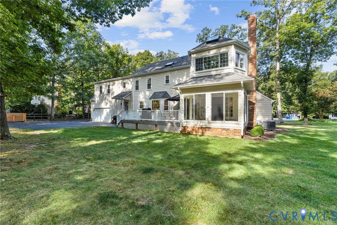 Expansive rear exterior featuring a multi-level deck, a sunroom with brick foundation, a two-story bay window element, and a prominent brick chimney
