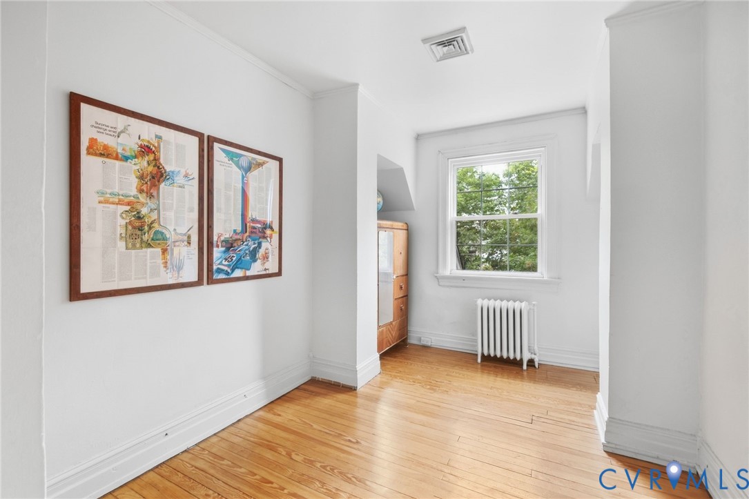 Hardwood flooring, painted white walls, white window frame, white baseboard trim, and a white radiator