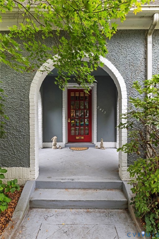 Arched entryway with brick surround, textured exterior finish, and a red paneled door