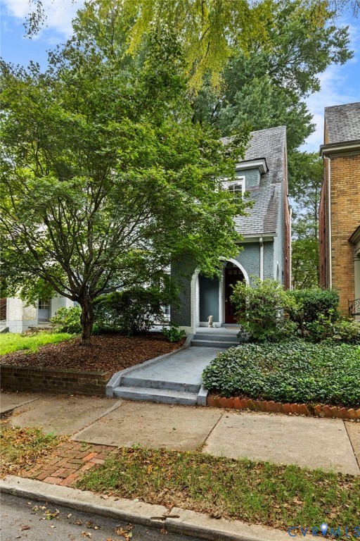 Stucco exterior with an arched entryway, dormer window, and mature landscaping
