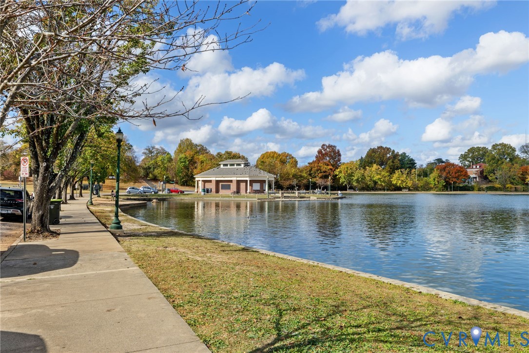 Lakeside property featuring a paved walkway, mature trees, and a distant pavilion