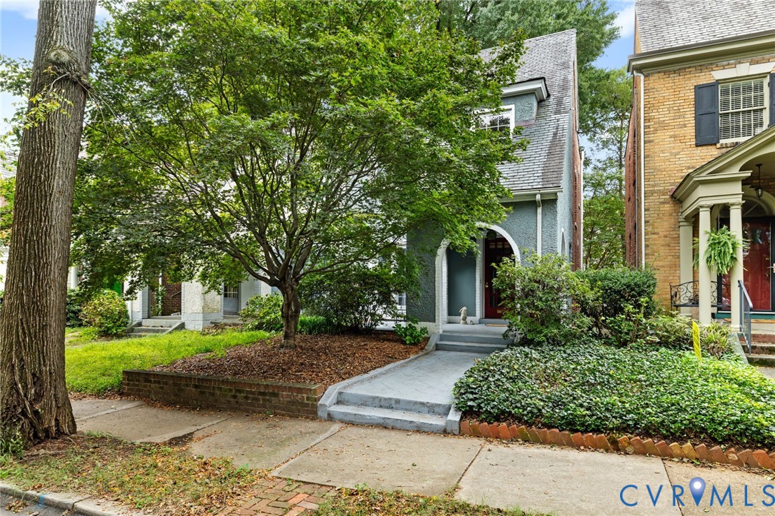 Front exterior featuring a gabled roofline, arched entry, mature trees, and established landscaping