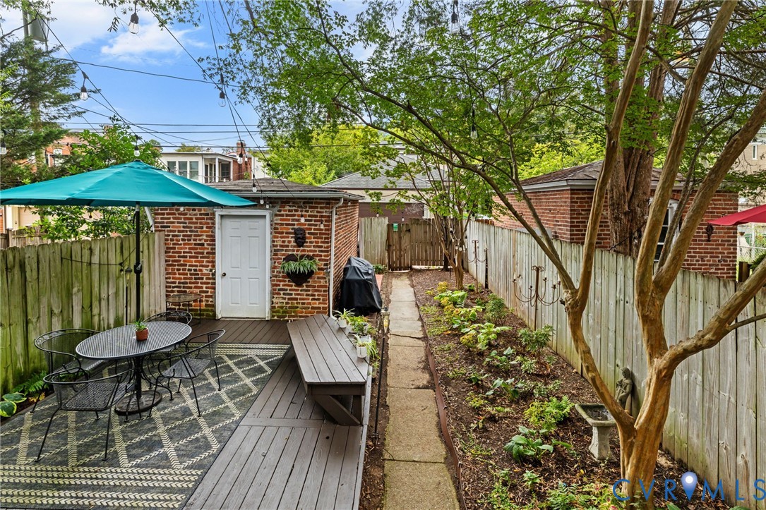 Expansive outdoor deck with built-in bench seating, brick-clad utility structure, wood privacy fencing, and established landscaping