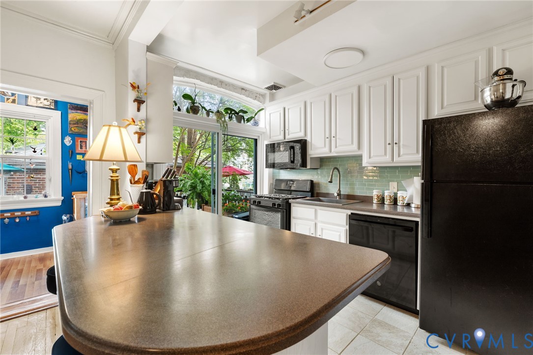 Kitchen featuring a kitchen island, white cabinetry, black appliances, a tile backsplash, and sliding glass doors
