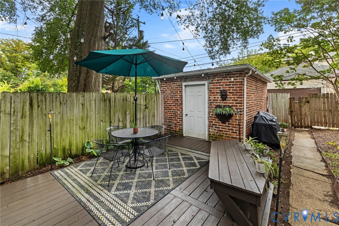 Outdoor deck with a brick-clad auxiliary building, string lighting, and a privacy fence