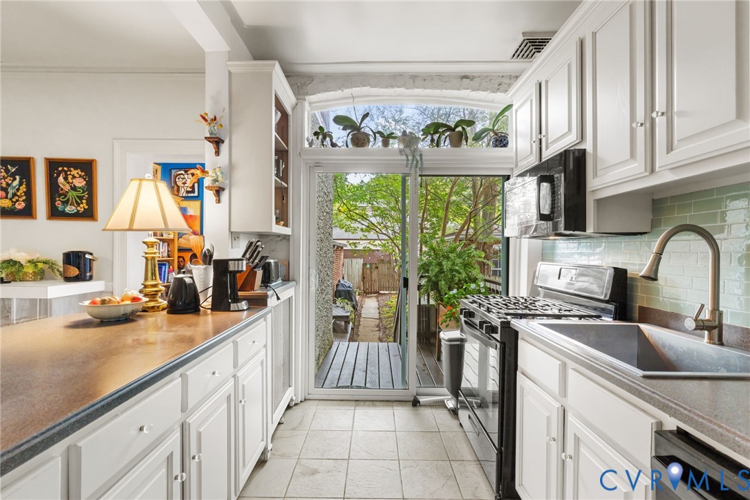 White cabinetry, tile flooring, glass tile backsplash, sliding glass door, and a built-in microwave