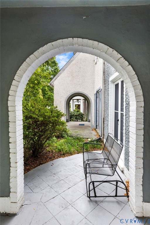 Arched brick entryway with a painted finish, leading to an exterior corridor featuring a patterned concrete patio