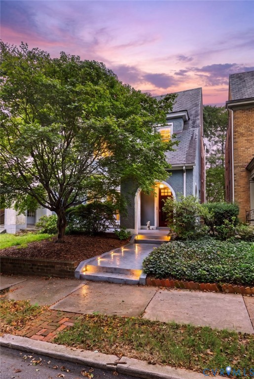 Stucco facade residence with an arched entry, prominent dormer window, and mature front landscaping