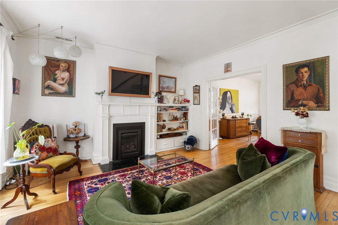 Hardwood flooring throughout, white crown molding, a built-in fireplace with a stone hearth, and integrated shelving