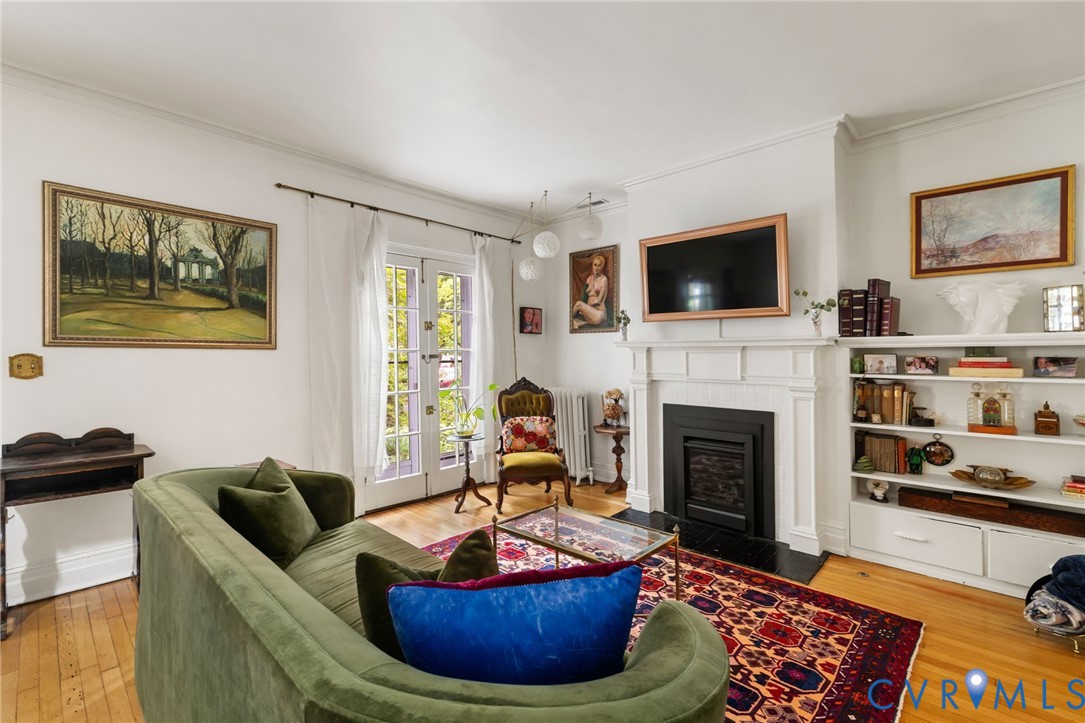 Hardwood flooring, white crown molding, built-in shelving, white double doors, and a decorative fireplace with a mantel