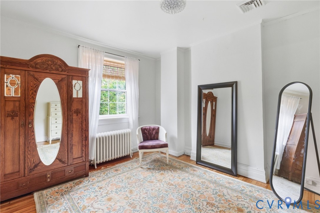 Hardwood flooring, painted white walls, single window with blinds, and crown molding