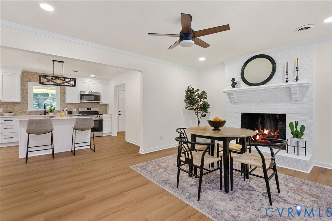 Wood-finish flooring throughout, white painted brick fireplace with mantel, recessed lighting, and a kitchen featuring white cabinetry, an island with countertop seating, and stainless steel appliances